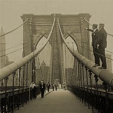 Black and white photo of a group of people walking on the Brooklyn Bridge
